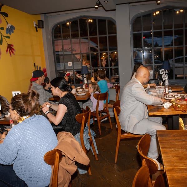 Diners enjoying meals at wooden tables in a vibrant La Taqueria restaurant with large windows.