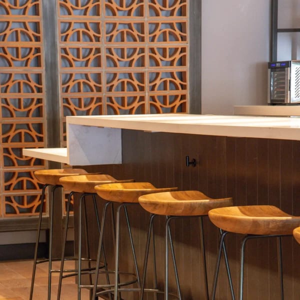 Modern bar area at La Taqueria with wooden stools, a light countertop, and decorative orange screens.