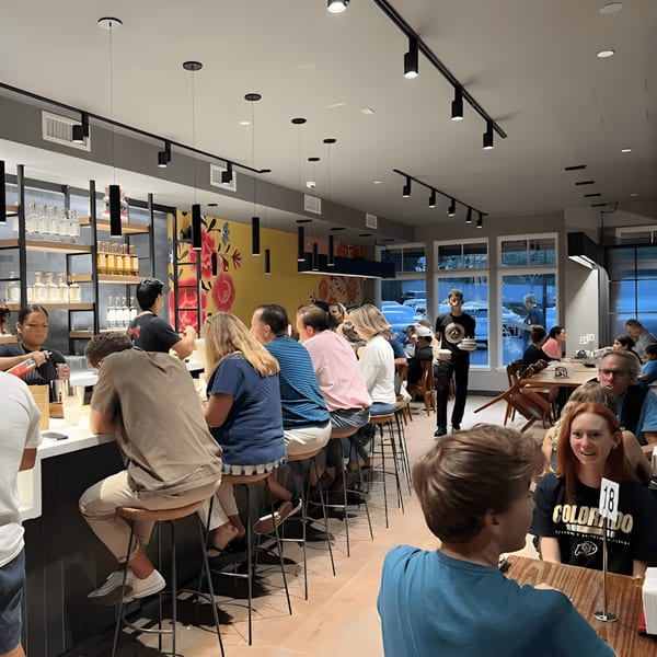 Diners seated at a long bar and tables in a brightly lit La Taqueria restaurant.