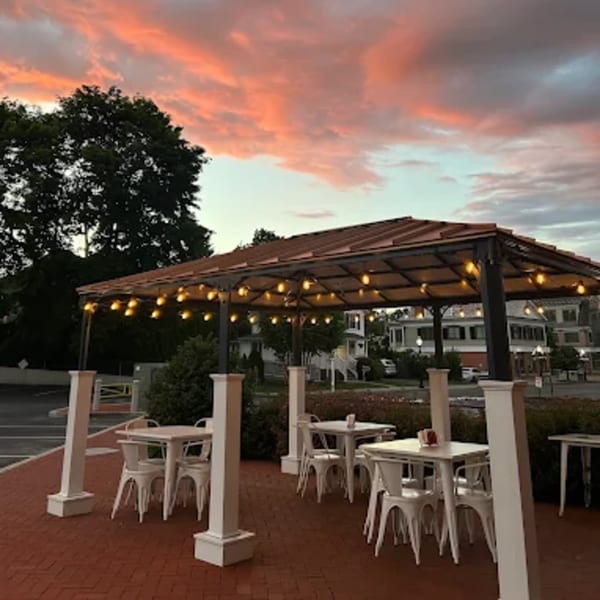 La Taqueria's outdoor patio with white tables and chairs under a lit canopy at sunset.
