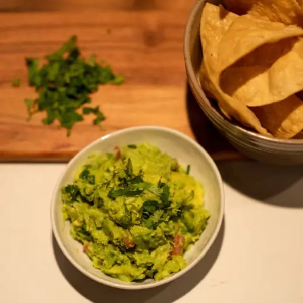 Fresh guacamole with cilantro and diced tomatoes, served with a bowl of tortilla chips.