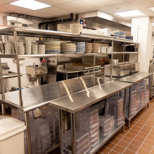 A clean, organized commercial kitchen with stainless steel counters, shelves, and cooking equipment.