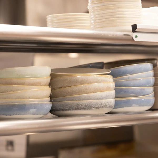Stacks of clean, colorful ceramic bowls and white plates on metal shelves in a restaurant kitchen.