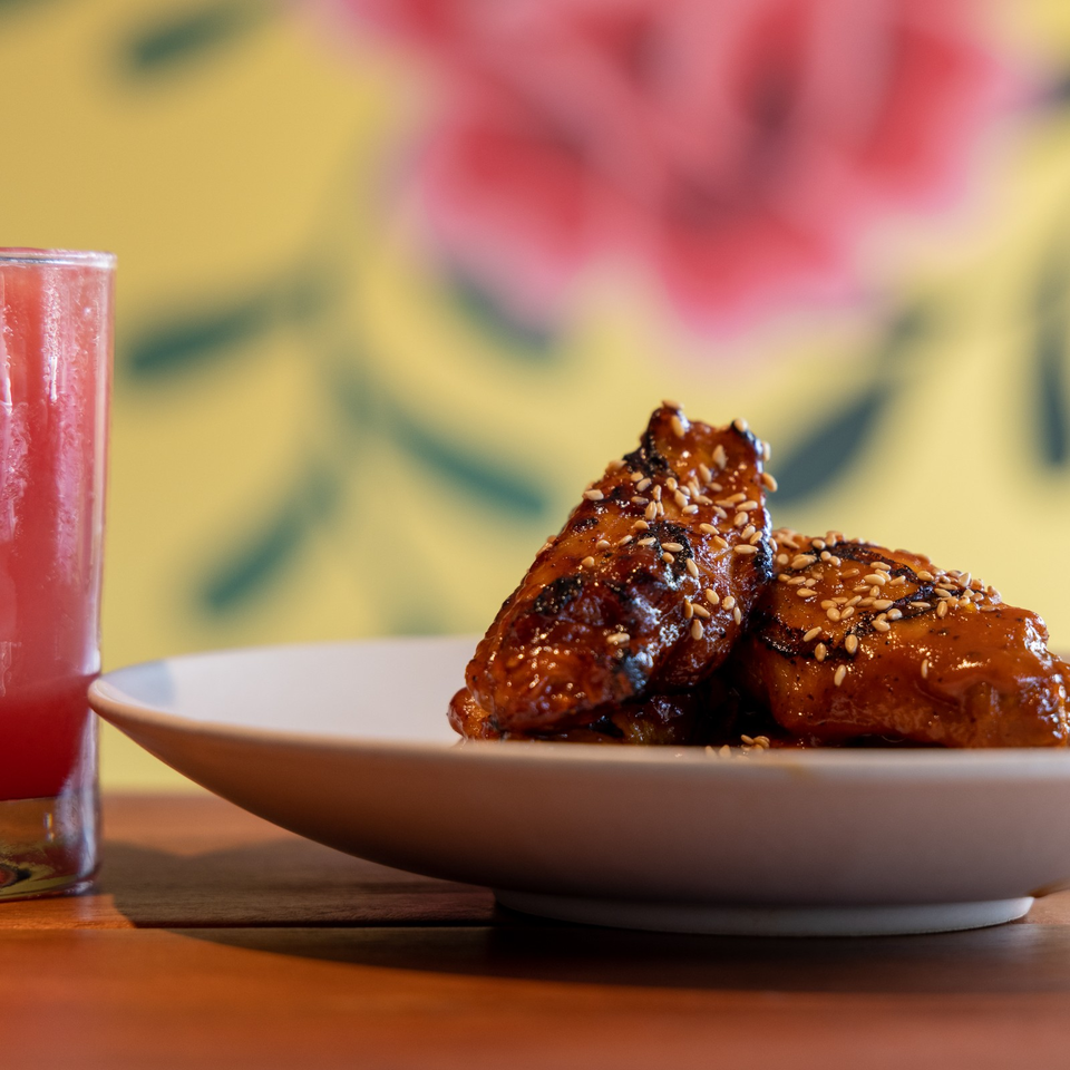 Glazed, sesame-sprinkled chicken wings piled on a white plate beside a red drink.