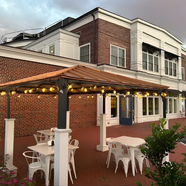 La Taqueria's outdoor patio with white tables and chairs under a lit gazebo, next to a brick building.