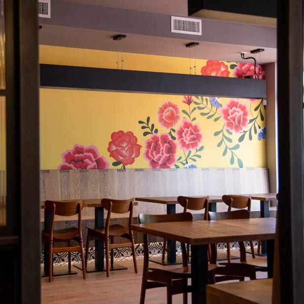 La Taqueria's dining room with a vibrant yellow wall mural featuring large red and blue flowers.