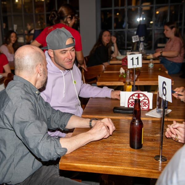 Two men conversing at a wooden table in a dimly lit La Taqueria restaurant.