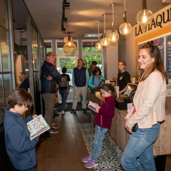Customers, including children, waiting in line at the counter of La Taqueria restaurant.