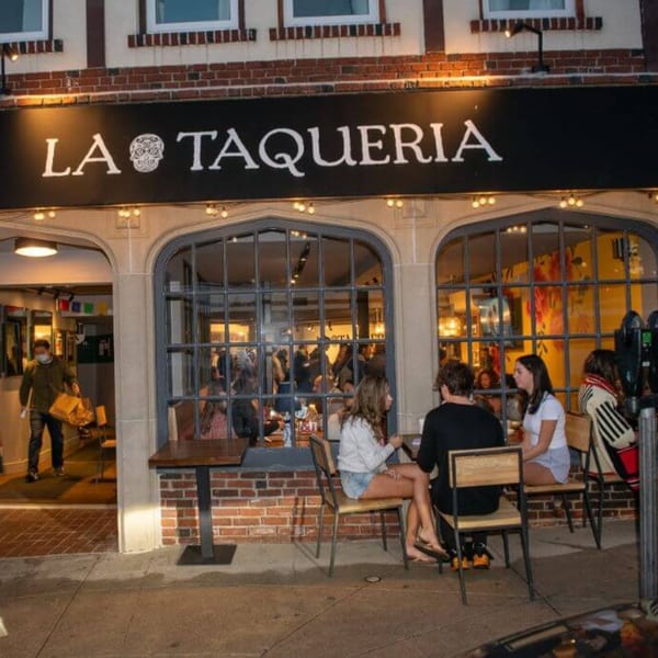 La Taqueria restaurant exterior at dusk, with patrons dining inside and outside on the patio.