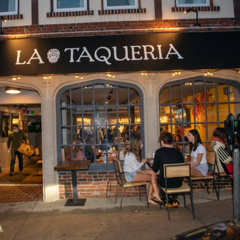 La Taqueria restaurant exterior at dusk, with patrons dining inside and outside on the patio.