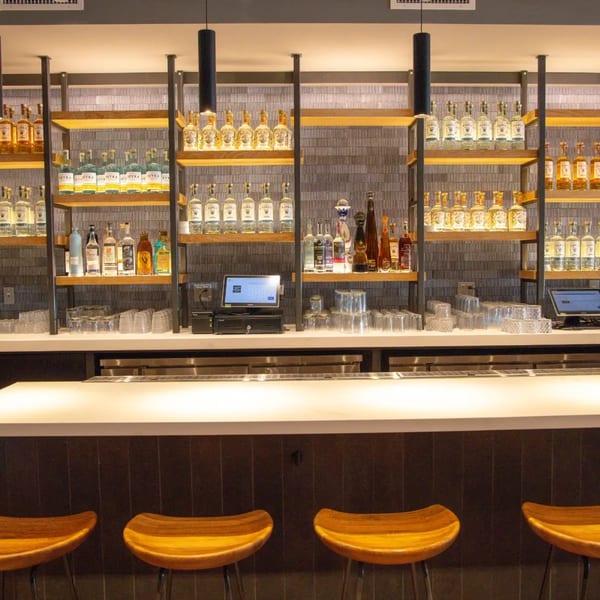 A well-stocked bar at La Taqueria with shelves of tequila bottles, glasses, and wooden stools.