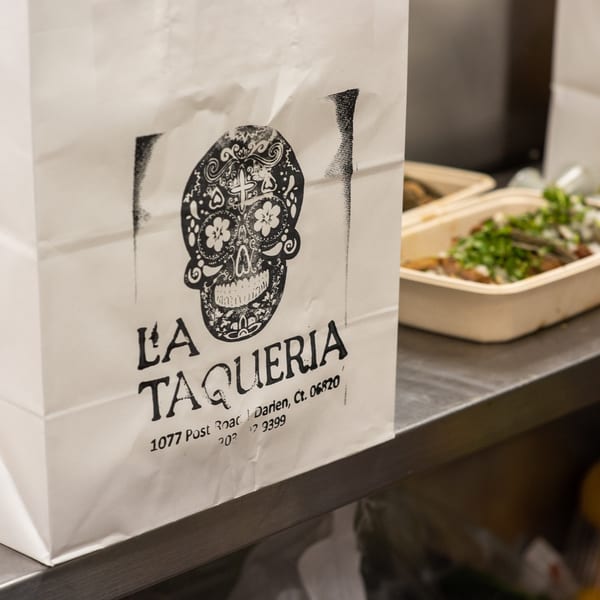 La Taqueria branded takeout bag with a sugar skull logo next to takeout containers of food.