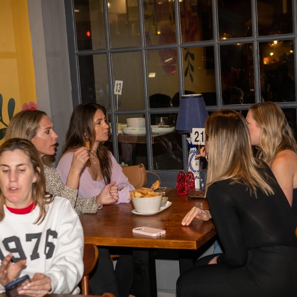 Women gather around a wooden table with a bowl of chips and a decorative bottle at La Taqueria.