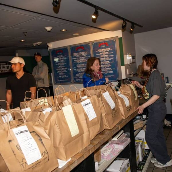 Customers waiting for their La Taqueria takeout orders, neatly arranged in brown paper bags on a counter.