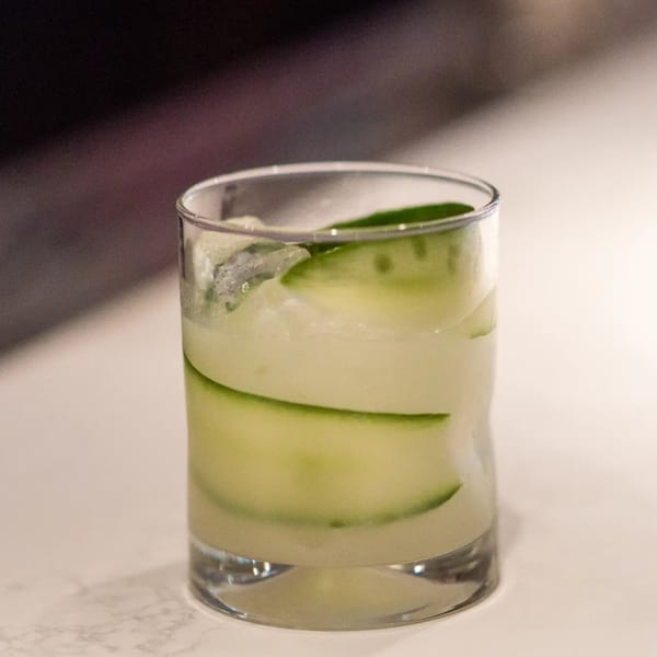 A refreshing cucumber margarita with ice in a clear glass on a white surface.
