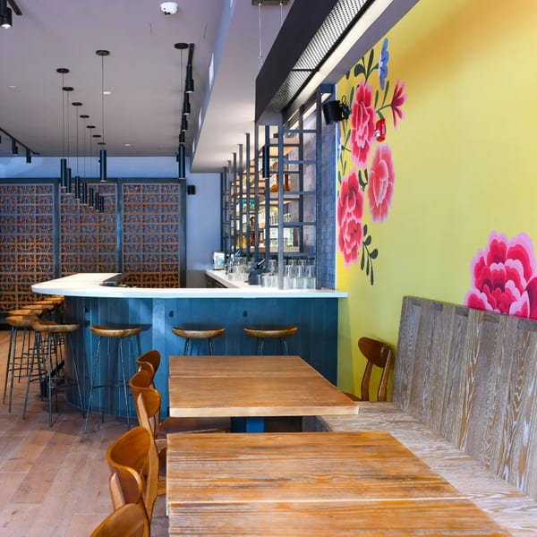 La Taqueria's vibrant interior with a blue bar, wooden tables, and a yellow wall with large pink floral murals.