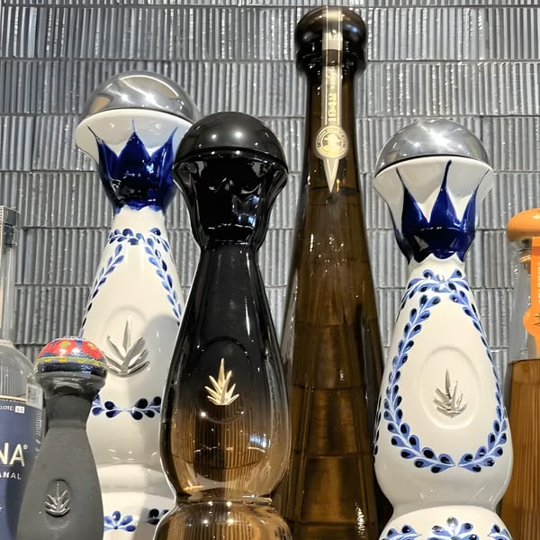 Assortment of decorative tequila bottles, some with blue and white designs, against a textured wall.
