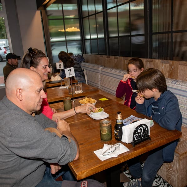 Family enjoying chips and guacamole at a wooden table in La Taqueria restaurant.