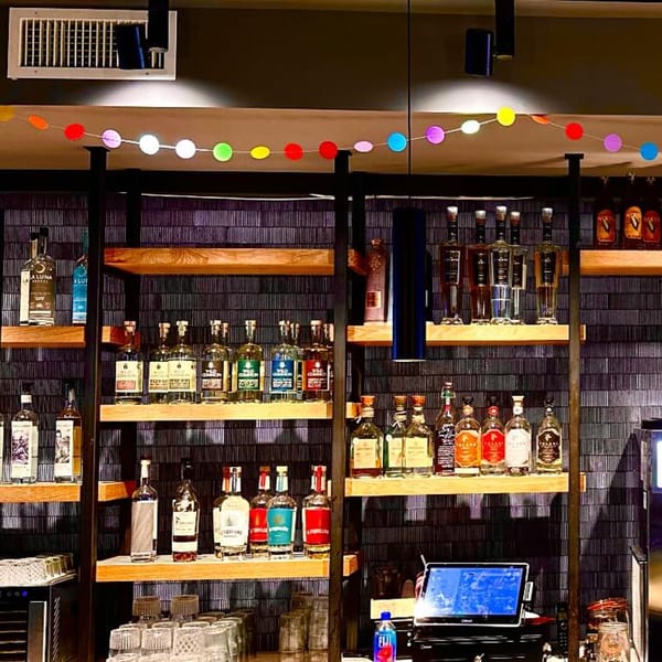 A bar at La Taqueria with shelves of tequila and mezcal bottles, and colorful papel picado.