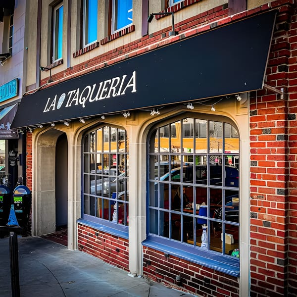 Exterior of La Taqueria restaurant with a black awning, brick facade, and arched windows.