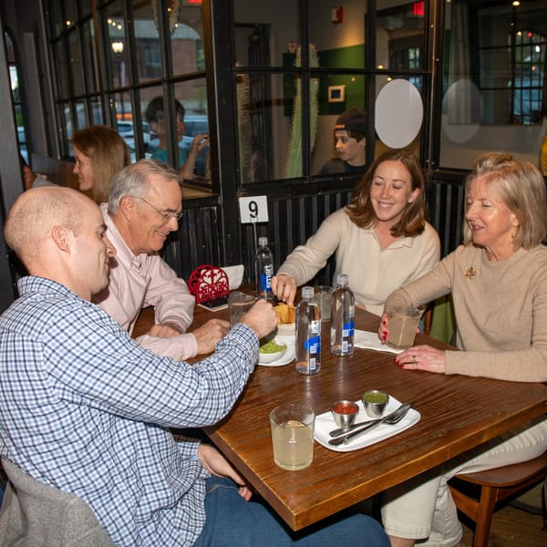 Four people enjoying drinks and chips with guacamole at a wooden table in La Taqueria.