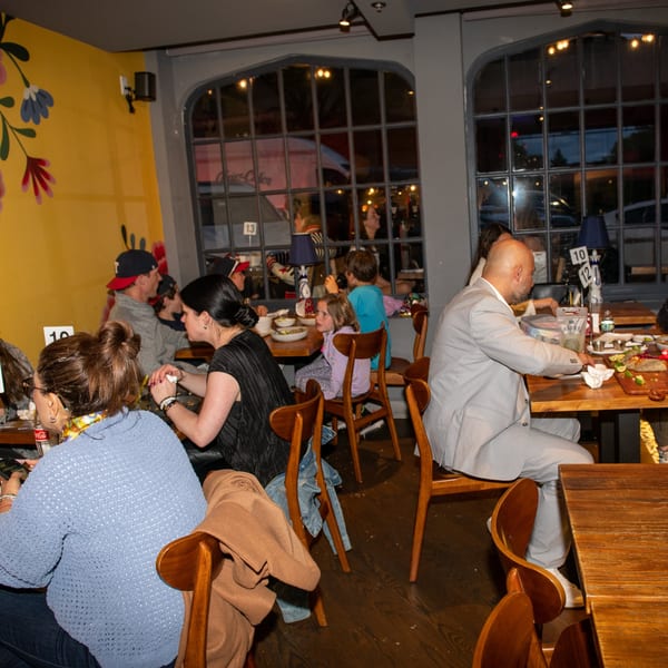 Diners enjoying meals at wooden tables in a vibrant La Taqueria restaurant with arched windows.