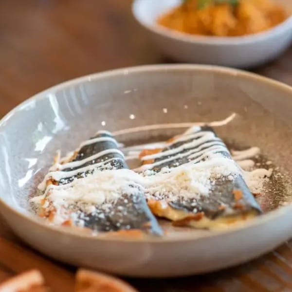 Two dark crepes drizzled with white sauce and powdered sugar in a light bowl at La Taqueria.
