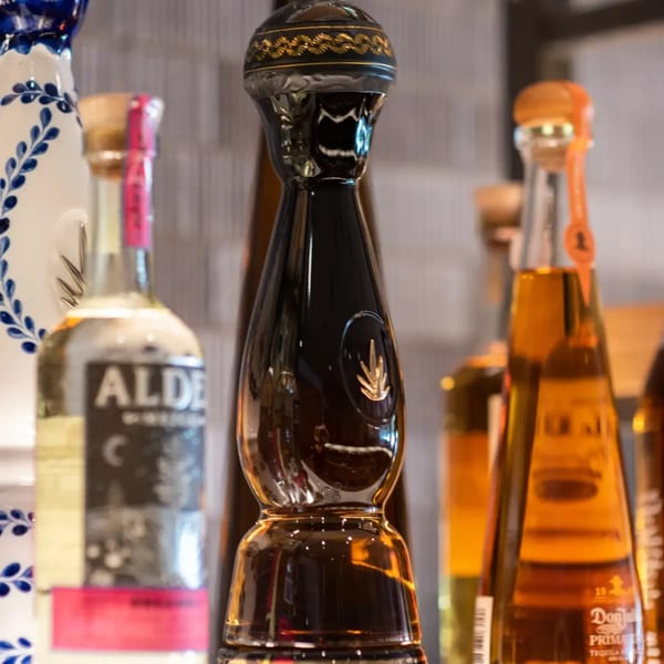 A close-up of various tequila bottles, including a distinctive black bottle with a gold agave emblem.